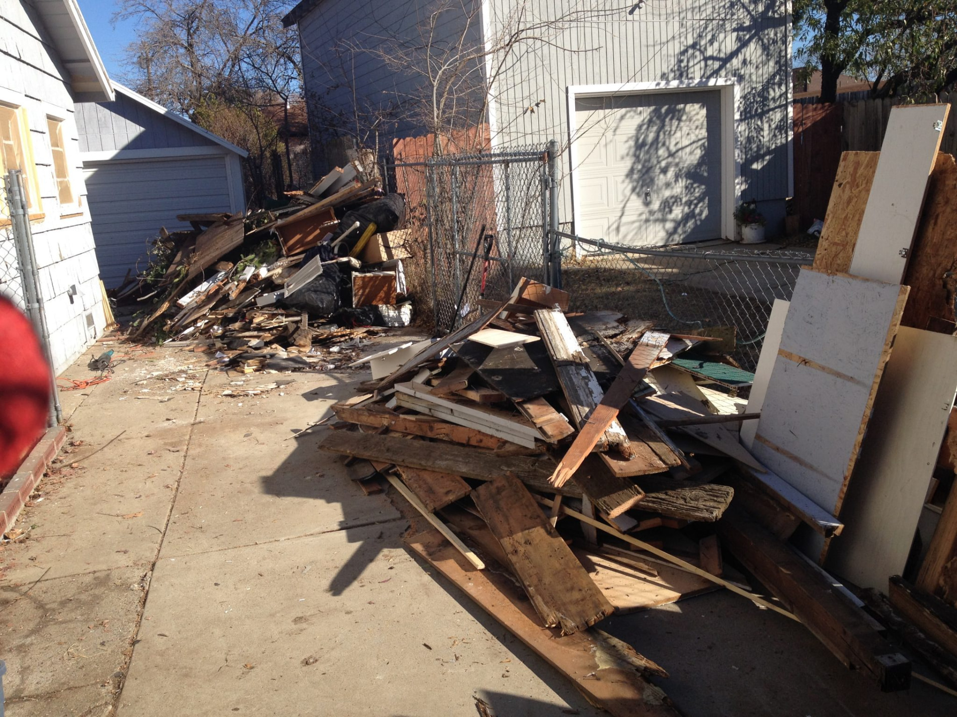 Demolition lumber, plywood, and construction debris piled in a backyard driveway